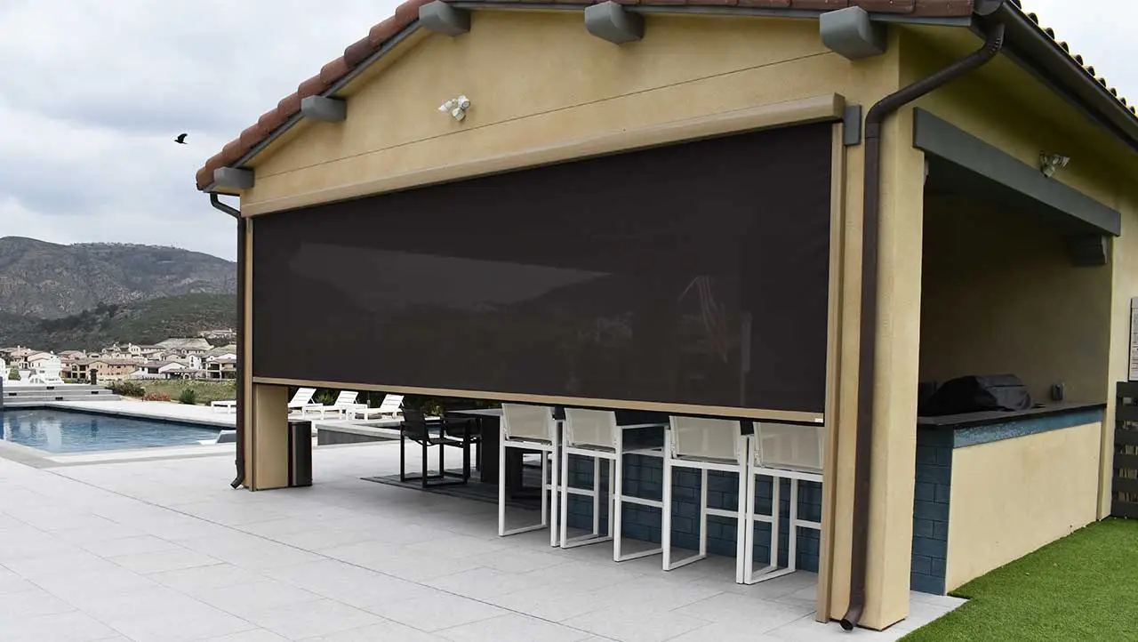 Luxury pool house patio with a motorized solar shade deployed over an outdoor kitchen